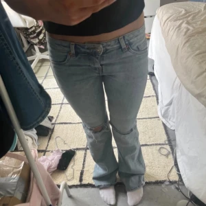 Ljusblå bootcut jeans - Säljer ett par ljusblå jeans med bootcut passform och låg midja. Jeansen har klassiska fem fickor och lätt slitna detaljer vid knäna. Perfekta för en avslappnad och trendig look.