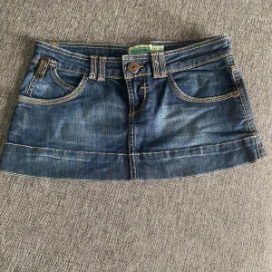 Low waist Jeanskjol - Snygg kort jeanskjol i blå denim med klassisk femficksdesign och knappstängning fram. Perfekt för en avslappnad stil. Märkesdetalj baktill ger en extra touch.