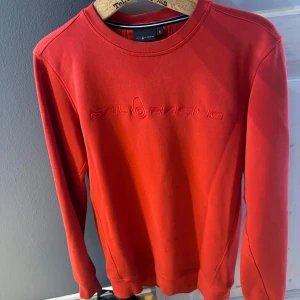 Röd tröja från Sail Racing - Säljer en snygg röd tröja från Sail Racing med broderad logga på framsidan. Tröjan har långa ärmar och en rund halsringning. Perfekt för en casual look.