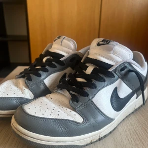 Nike Dunk i grått och vitt Storlek 43 - Säljer ett par klassiska Nike Dunk sneakers i grått och vitt. Köpte dom för 1700kr, storlek 43, box följer ej med,  skicket är helt okej förutom att tyget gått upp vid kanten av skon (bild 3). Några funderingar eller frågor så är det bara o skriva 