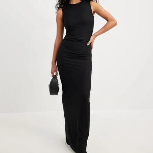Svart långklänning från NA-KD - Svart långklänning från NA-KD med en tight passform och ärmlös design. Klänningen har en slits på baksidan. Materialet är mjukt och följsamt.