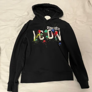 Svart hoodie från Dsquared2 - Säljer en svart hoodie från Dsquared2 med färgglatt tryck på framsidan. Hoodien har en klassisk design med dragsko i huvan och ribbade muddar vid ärmslut och nederkant. Perfekt för en avslappnad stil. Pris sänks vid snabbaffär. 