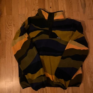 Randig fleece från Converse - Säljer en cool randig fleece från Converse i färgerna blå, grön, gul och orange. Tröjan har en halv dragkedja framtill och långa ärmar. Perfekt för kyliga dagar!