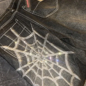 Svarta jeans med spindelnätsdesign - Svarta ”outwashed” baggy jeans med spindelnäts”mönster” på baksidan. Storleken är S men passar nog alla, riktigt snygga och oanvända med lapp kvar.
