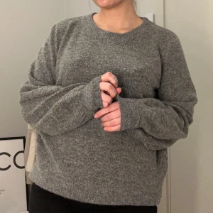 Grå stickad tröja från Soyaconcept - Mysig grå stickad tröja från Soyaconcept med en klassisk design. Perfekt för kyliga dagar med sin mjuka och bekväma passform. Tröjan har långa ärmar och en rund halsringning.