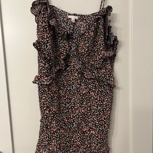 Blommig klänning från H&M - Säljer en söt blommig klänning från H&M med volangdetaljer. Klänningen har smala axelband och ett färgglatt mönster i rosa, vit och svart. Perfekt för sommarens alla tillfällen!