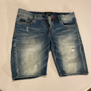 Blå jeansshorts från SuperDry - Snygga blå jeansshorts från SuperDry med en vintage look och slitna detaljer. De har en slim passform och klassisk femficksdesign. Perfekta för en avslappnad stil.