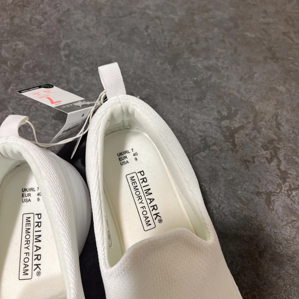 Säljer ett par vita slip-on sneakers från Primark med memory foam för extra komfort. Skorna har en enkel och stilren design utan snörning, vilket gör dem lätta att ta på och av. Perfekta för en avslappnad stil.. Kengät.
