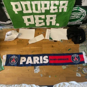 Paris Saint-Germain halsduk - Snygg halsduk med Paris Saint-Germain logga. Ena sidan är blå med vit text och röd detalj, medan andra sidan är röd med blå text. Perfekt för att visa ditt stöd för laget!