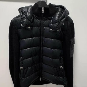 Svart cardigan jacka från Moncler - Säljer en svart cardigan jacka från Moncler med quiltade detaljer och huva. Jackan har dragkedja framtill och långa ärmar. Perfekt för kyligare dagar. ENDAST BYTEN!!