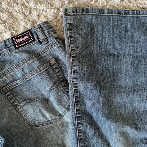 Lågmidjade blå jeans från Bubblegum - Snygga blå jeans från Bubblegum med klassisk femficksdesign och en stjärnformad knappdetalj. Fina rosa detaljer på. Innerbenslängd: 78 cm. Midjemått rakt över: ca 37. Midjehöjd: 19 cm. Perfekt lågmidjade. Lite slitna längst ned. Kan skicka bild på hela privat, fick inte plats i bilderna här