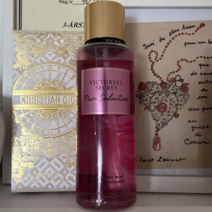 Victoria's Secret Pure Seduction Body Mist - Säljer en Victoria's Secret Pure Seduction body mist med en doft av saftig plommon och krossad fresia. Flaskan är rosa med en gyllene kork och rymmer 250 ml, lite är använt. Perfekt för en fräsch och blommig doft hela dagen.