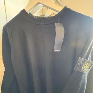 Stone Island sweatshirt - SVART RIBBSTICKAD TRÖJA MED BADGE från Stone Island med deras ikoniska märke på ärmen. Tröjan har en rund halsringning och är tillverkad i ett mjukt material. Perfekt för en stilren look.