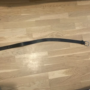 Svart bälte med silverfärgat spänne - Snyggt svart bälte med ett stilrent silverfärgat spänne. Perfekt för att ge en klassisk touch till din outfit. Passar både till jeans och kostymbyxor.