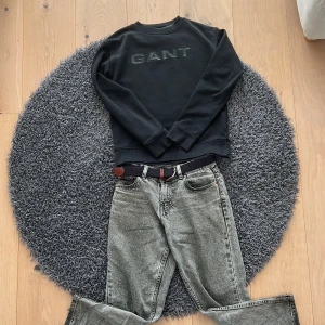 Svart sweatshirt från GANT - Säljer en stilren svart sweatshirt från GANT med deras logga diskret broderad på bröstet. Tröjan har långa ärmar och ribbade muddar vid ärmslut och nederkant. Perfekt för en avslappnad look.