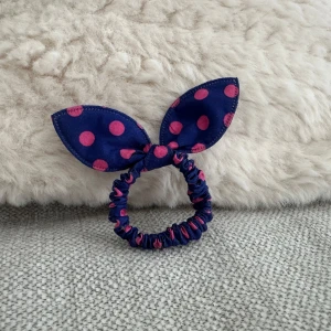 Blå scrunchie med prickar - Snyggt blått  scrunchie med rosa prickar och kaninöron. Perfekt för att ge en lekfull touch till din outfit. Elastiskt band för bekväm passform.