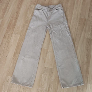 Högmidjade beiga jeans - Snygga beige byxor från Monki med raka ben och hög midja. De har en normal passform och är perfekta för en avslappnad stil. Byxorna har fickor både fram och bak samt en knapp och dragkedja i gylfen.