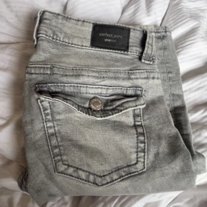 Grå jeans från Gina - Snygga grå jeans från Perfect Jeans med en klassisk femficksdesign. De har en knapp och dragkedja framtill och är perfekta för en avslappnad stil. Använts ett par gånger men fortfarande i ett bra skick