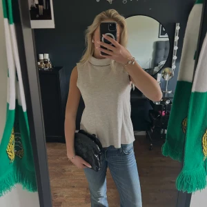 Beige ärmlös polotopp - Säljer en stilren beige ärmlös polotopp. Perfekt för en avslappnad men ändå elegant look. Toppen har en mjuk och bekväm passform.