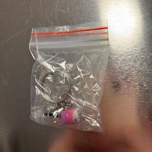 Nyckelring med rosa och vit berlock - Söt nyckelring med en liten berlock i form av en rosa och vit figur. Perfekt som en charmig accessoar till dina nycklar eller väska.