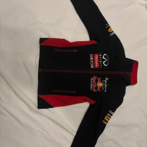 Svart racingjacka från Pepe Jeans - Säljer en svart racingjacka för barn från Pepe Jeans med Red Bull-loggor. Jackan har röda detaljer och dragkedja framtill. Perfekt för racingfans! 🏎️Inga defekter och nypris 1200 kr