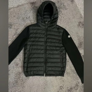 Moncler Cardigan - Snygg svart Cardigan från Moncler med huva och dragkedja. Jackan har långa ärmar och är perfekt för kyligare väder. Den quiltade designen ger en stilren look.