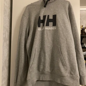 Grå helly hansen hoddie - Grå hoddie med en ficka på magen. Den är i ett väldigt bra sick å nästan aldrig använd. Säljer den då den inte kommer till användning längre. Ny pris 700kr