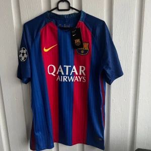 Blå och röd FC Barcelona fotbollströja - Säljer en officiell FC Barcelona fotbollströja från Nike med korta ärmar. Tröjan har ett randigt mönster i blått och rött med gula detaljer. Den har tryck med 'Qatar Airways' på framsidan och 'Neymar Jr 11' på baksidan. Perfekt för fans av laget!