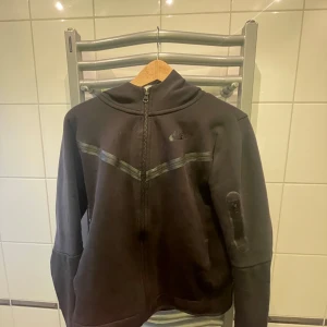 Svart fleecejacka med dragkedja - Säljer en svart fleecejacka med dragkedja och huva. Jackan har långa ärmar och en stilren design med diskreta detaljer. Perfekt för kyliga dagar.