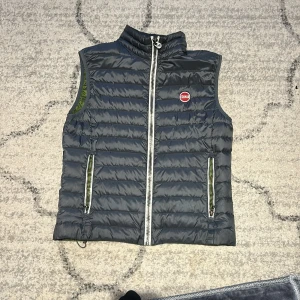 Grå quiltad dunväst från Colmar - Säljer en stilren grå dunväst från Colmar med dragkedja och hög krage. Västen har en snygg grön insida och två praktiska fickor med dragkedjor. Perfekt för lager-på-lager under kyliga dagar. Defekt på baksidan som är rätt smidigt ihopsydd, svår att upptäcka. Annars nyskick. Storlek 48/S