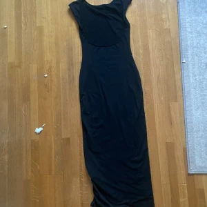 Svart långklänning - Elegant svart långklänning med en tight passform. Klänningen har korta ärmar och har öppen rygg. Perfekt för en stilren och klassisk look.