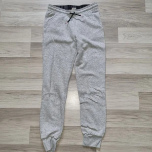 Grå mjukisbyxor från H&M - Säljer ett par bekväma grå mjukisbyxor från H&M. Byxorna har en elastisk midja med svart snörning och ribbade muddar vid bensluten. Perfekta för en avslappnad stil.