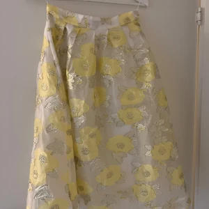 Blommig kjol från Baum und Pferdgarten - Säljer en vacker långkjol från Baum und Pferdgarten med ett blommigt mönster i gult och silver. Kjolen är tillverkad i polyester och polyamid, vilket ger den en fin glans. Perfekt för att lysa upp garderoben med lite färg och stil! Längd 73 cm