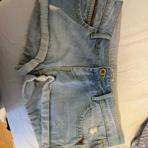 Ljusblå jeansshorts från River Island - Snygga ljusblå jeansshorts från Wrangler med slitna detaljer och uppvikta ben. Perfekta för en avslappnad sommarlook. Klassisk femficksdesign och knappgylf. Säljer då dom är förstora på mig😢