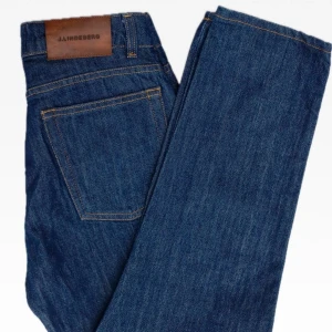 J.Lindeberg Jeans strl w27 - J.Lindeberg Study jeans  Passform: hög midja, raka ben  Färg: Mörkblå denim  Material: 100% bomull  Skick: Mycket bra skick, skulle gissa på oanvända  nästan!   Storlek: 27/30   Mått: Midja: 35,5cm Innerlår: 66cm Benöppning: 16cm