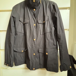 Svart jacka från Peak Performance - Säljer en stilren svart jacka från Peak Performance. Jackan har långa ärmar och flera praktiska fickor med knappar. Perfekt för en stilren look.