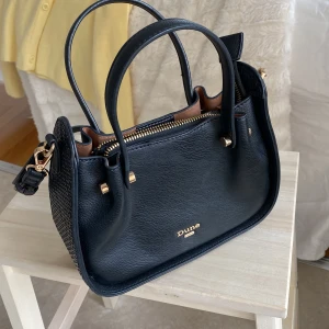 Svart handväska från Dune - Snygg svart handväska från Dune med justerbar axelrem och praktiska handtag. Väskan har en elegant design med guldfärgade detaljer och dragkedja för säker förvaring