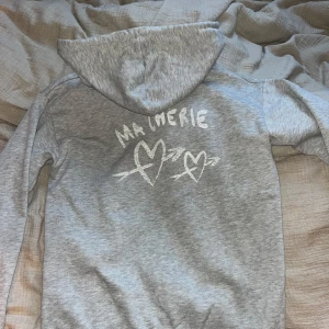Grå hoodie från Gina Tricot - Säljer en grå hoodie från Gina Tricot med texten 'MA CHERIE' på bröstet och ett hjärtmönster på ryggen. 🩶