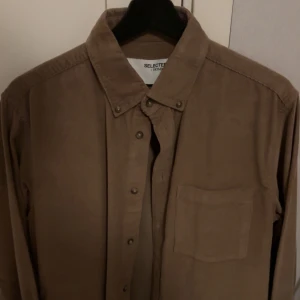 Beige overshirt från Selected Homme - Snygg beige overshirt från Selected Homme i ett mjukt material. Skjortan har långa ärmar och knappar framtill samt en bröstficka. Perfekt för lager-på-lager-stil. Helt oanvänd!