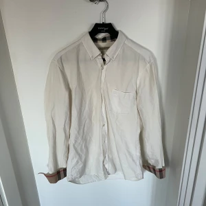 Burberry skjorta - Säljer en riktigt snygg vit burberry skjorta i storlek M. Äkthetsbevis följer med vid köp. Skick 8/10 men saknar någon knapp men ett ganska enkelt fix med extraknappar. Hör av er vid intresse. Pris är diskuterbart