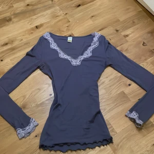  Y2K lila spelstopp  - Säljer en stilren lila långärmad topp från Calida med vacker spetsdetalj vid halsringning och ärmslut. Toppen har en ribbad struktur och en feminin passform. Den har hål på sina stället men går säkert att sy ihop.