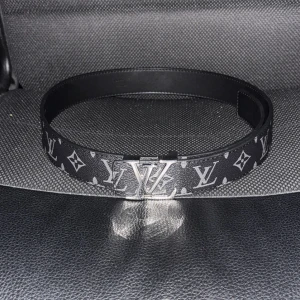 Svart bälte från Louis Vuitton - Snyggt svart bälte från Louis Vuitton med det ikoniska LV-mönstret och ett stilrent silverfärgat spänne. Perfekt för att ge din outfit en lyxig touch. Kommer med en praktisk förvaringspåse. Pris kan diskuteras