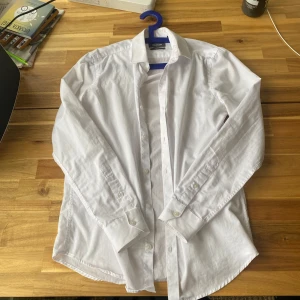 Vit skjorta från Dressmann - Säljer en klassisk vit skjorta från Dressmann i slim fit. Skjortan har långa ärmar och knappar framtill. Perfekt för en stilren look.
