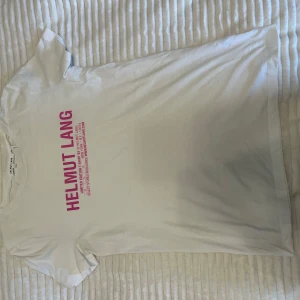 Vit t-shirt från Helmut Lang - Säljer en vit t-shirt från Helmut Lang med rosa texttryck på framsidan. T-shirten är kortärmad och gjord av bomull.💕