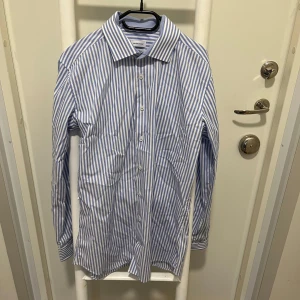 Blå- och vitrandig skjorta - Snygg blå- och vitrandig skjorta med klassisk krage och knappar framtill. Storlek M