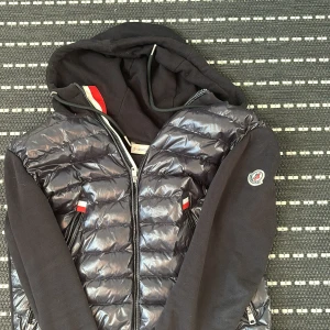 Svart pufferjacka med huva från Moncler - Svart monclerjacka använd några gånger men är tyvärrr för liten för mig skicket är bra och det är en ganska ovanlig modell. Jackan sitter som storlek S