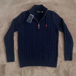 Mörkblå Ralph Lauren Kabelstickad Halv Zip Tröja - Helt ny mörkblå kabelstickad Ralph Lauren Halv zip. Tröjan är i Strl L men kan eventuellt passa M då ullen är stretchig. Tags tillkommer. Vid frågor eller funderingar skicka ett pm, Mvh