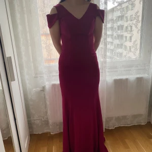 Vinröd långklänning från Newness - Säljer en elegant vinröd långklänning från Newness med figurnära passform och v-ringad hals. Klänningen har korta, markerade ärmar och är tillverkad i polyester med stretch därav passar någon storlek större också. Färgen är nära burgundy. Perfekt för festliga tillfällen! Säljes för att den inte har kommit till användning annars har den aldrig använts!