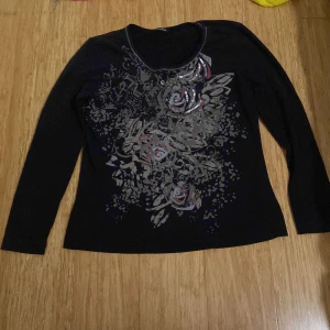 Svart långärmad topp med blommigt mönster från Gerry Weber - Snygg svart långärmad topp från Gerry Weber med blommigt mönster och diskreta paljettdetaljer framtill. Perfekt för dig som vill ha något stilrent men ändå med lite extra detaljer.