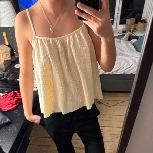 Beige plisserad linnetopp med smala axelband - Säljer en luftig beige linnetopp med smala axelband och snyggt korsade band i ryggen